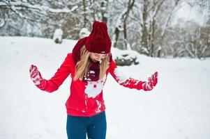 ragazza bionda in sciarpa rossa, cappello e maglione di Babbo Natale in posa al parco il giorno d'inverno. foto