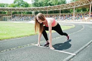 fitness ragazza sportiva in abbigliamento sportivo allo stadio di sport all'aria aperta. donna sexy felice che corre sul tapis roulant della pista di atletica sullo stadio. foto