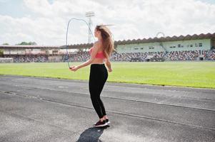 fitness ragazza sportiva in abiti sportivi in uno stadio di calcio sport all'aria aperta. allenamento donna sexy felice e saltare con la corda. foto