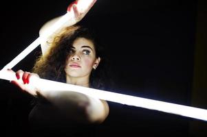 bruna riccia modello plus size con due lunghe lampade a led in camera nera. foto