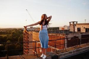 ritratto di una bella ragazza in abbigliamento casual in posa sul tetto con il cappello in mano al tramonto. foto