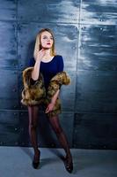 elegante ragazza bionda indossare su pelliccia e vestito combinato contro la parete d'acciaio in studio. foto