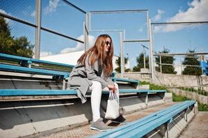 ragazza in cappotto grigio con occhiali da sole al piccolo stadio di strada. foto