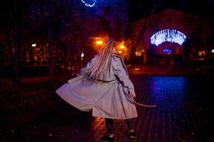 ragazza con i dreadlocks che cammina di notte per la strada della città contro le luci della ghirlanda. foto