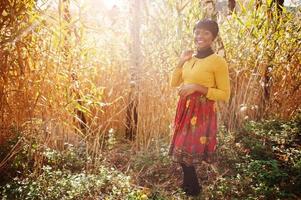 ragazza afroamericana in abito giallo e rosso al parco autunnale dorato. foto