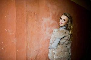 ragazza bionda al cappotto di pelliccia poste contro il vecchio muro arancione. foto
