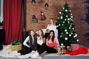 quattro ragazze carine amiche indossano maglioni caldi, pantaloni neri e cappelli di Babbo Natale contro l'albero di Capodanno con decorazioni natalizie in studio. foto