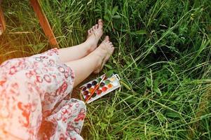 foto ravvicinata di gambe femminili sull'erba alta insieme alla tavolozza dell'acquerello.