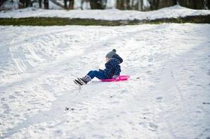 bambina carina con slitte a piattino all'aperto in una giornata invernale. foto