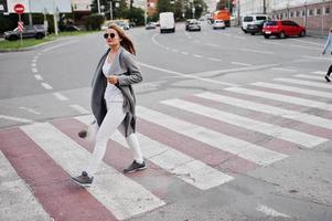 ragazza in cappotto grigio con occhiali da sole e borsetta che cammina sul passaggio pedonale. foto