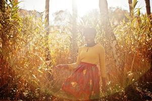 ragazza afroamericana in abito giallo e rosso al parco autunnale dorato. foto