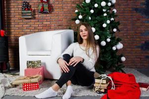 ragazza carina indossare maglioni caldi, pantaloni neri contro albero di capodanno con decorazioni natalizie in studio. foto