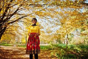 ragazza afroamericana in abito giallo e rosso al parco autunnale dorato. foto