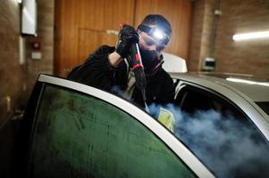 uomo in uniforme e respiratore, lavoratore del centro di autolavaggio, pulizia degli interni dell'auto con pulitore a vapore caldo. concetto di dettagli dell'auto. foto