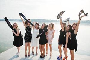 un gruppo di 8 ragazze indossano il nero e 2 spose alla festa di addio al nubilato contro la spiaggia soleggiata. foto