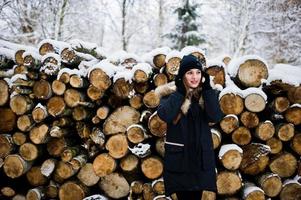 bella ragazza bruna in abiti caldi invernali. modello su giacca invernale e cappello vicino a ceppi di alberi. foto