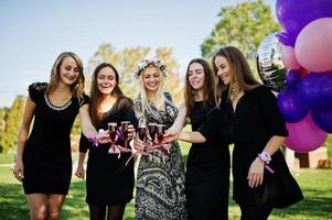 cinque ragazze indossano il nero con palloncini che bevono champagne rosso all'addio al nubilato. foto