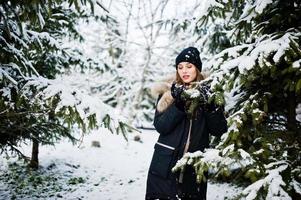 bella ragazza bruna in abiti caldi invernali. modello su giacca invernale e cappello vicino ai pini. foto