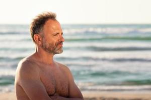 ritratto di un uomo barbuto senza camicia di profilo sullo sfondo del mare nel tramonto estivo foto