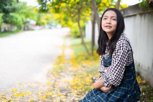 giovane ragazza seduta su una panchina a leggere un libro sotto un bellissimo albero. foto