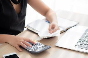 donna della mano del primo piano che calcola le spese della famiglia e scrive il taccuino sulla scrivania, la ragazza che controlla la fattura e lo stress e la nota, la preoccupazione femminile del debito e delle tasse, la finanza e il concetto di business. foto