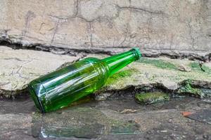 una bottiglia con una bevanda alcolica scaduta gettata in una pozzanghera per strada. il problema dell'alcolismo nella società foto