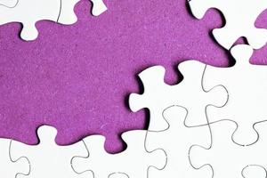 puzzle bianco con alcuni pezzi mancanti su sfondo viola. copia spazio. foto