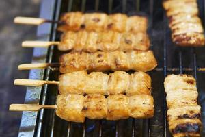 primo piano di spiedini di salmone alla griglia barbecue su bastoncini di legno, mercato tailandese di cibo di strada foto