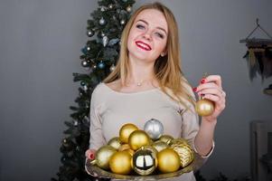 ragazza bionda carina su abito beige contro albero di capodanno con palline dorate di capodanno in studio. Buone vacanze. foto