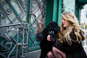 eleganza ragazza bionda in pelliccia abbraccia un piccolo cane nero. foto