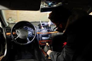 uomo in uniforme e respiratore, lavoratore del centro di autolavaggio, pulizia della spazzola per la pulizia degli interni dell'auto. concetto di dettagli dell'auto. foto