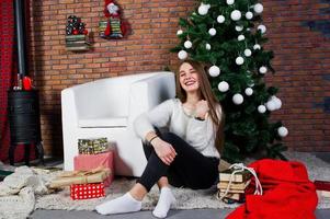 ragazza carina indossare maglioni caldi, pantaloni neri contro albero di capodanno con decorazioni natalizie in studio. foto