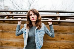 ritratto di ragazza riccia bruna in giacca di jeans contro la parete di legno. foto