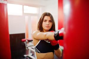 giovane bella donna, indossa guanti da boxe facendo esercizi e lavorando sodo in palestra e godendosi il suo processo di allenamento. foto