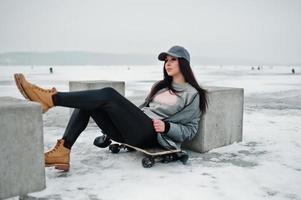 elegante ragazza bruna con berretto grigio, casual street style con skateboard in giornata invernale. foto