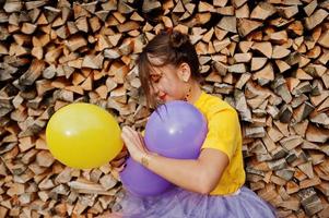 giovane ragazza divertente con trucco luminoso, indossare su camicia gialla con palloncini colorati su sfondo di legno. foto