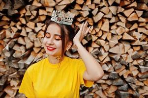 giovane ragazza divertente con trucco luminoso, come la principessa delle fiabe, indossa una camicia gialla e una corona su sfondo di legno. foto