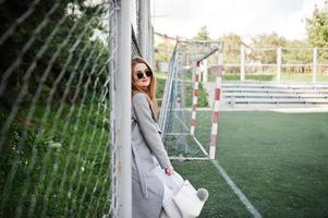 ragazza in cappotto grigio con occhiali da sole al piccolo stadio di strada. foto