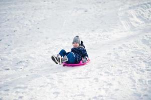 bambina carina con slitte a piattino all'aperto in una giornata invernale. foto