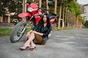 ritratto di una donna fresca e fantastica in abito e giacca di pelle nera seduta su una bella moto rossa. foto