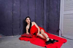 ragazza bruna in abito rosso posato vicino alla decorazione del nuovo anno in studio. foto