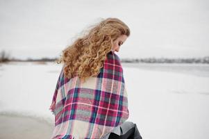 ragazza bionda riccia in plaid a scacchi contro il lago ghiacciato al giorno d'inverno. foto