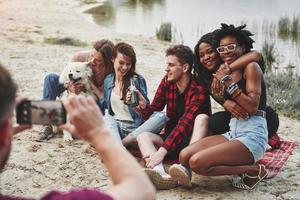 aspetta, mi sto concentrando un gruppo di persone fa un picnic sulla spiaggia. gli amici si divertono durante il fine settimana foto