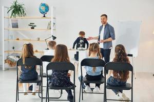 guardando il ragazzo con il microscopio che è sul tavolo. gruppo di bambini studenti in classe a scuola con l'insegnante foto