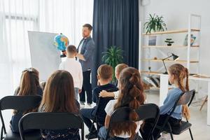 lezione di geografia con il globo in mano. gruppo di bambini studenti in classe a scuola con l'insegnante foto