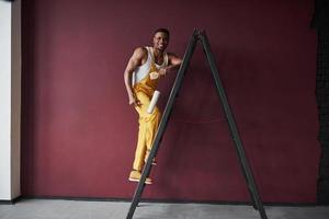 sulla scala. il giovane lavoratore afroamericano in uniforme gialla ha un lavoro foto