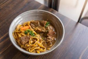 tagliatelle con spezzatino di maiale e verdure in una ciotola servite su tavola di legno, spaghetti con carne. foto