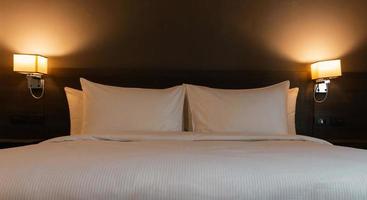 cuscini bianchi e coperta a letto con la luce delle lampade di notte foto