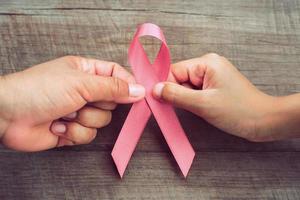concetto di assistenza sanitaria e medicina. due mani che tengono nastro rosa su legno. consapevolezza del cancro al seno segno di speranza foto