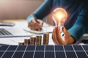 donna d'affari che tiene lampadina con turbina su monete e pannello solare. concetto di risparmio energetico e contabilità finanziaria foto